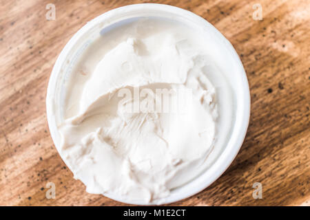 Closeup of small tub plastic container of white cream cheese on table, flat top view down macro Stock Photo