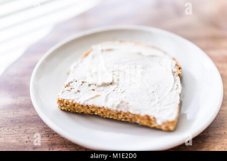 Closeup of slice piece of whole wheat sprouted toasted grain bread on plate with white cream cheese spread on table macro Stock Photo