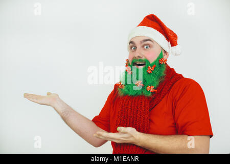 Santa Clause in red clothes with green beard decorated with red bows shows something Stock Photo