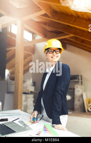 very pretty young female architect wearing yellow helmet is planning a loft in a house Stock Photo