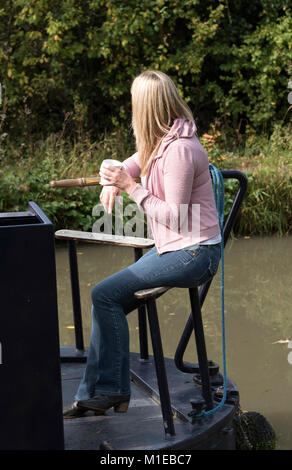 Woman using the tiller to steer a narrowboat along an English canal Stock Photo