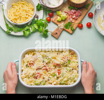 Female hand holding pasta casserole with tomato, bacon and cheese, top view. American style hearty macaroni pasta in cheesy sauce Stock Photo
