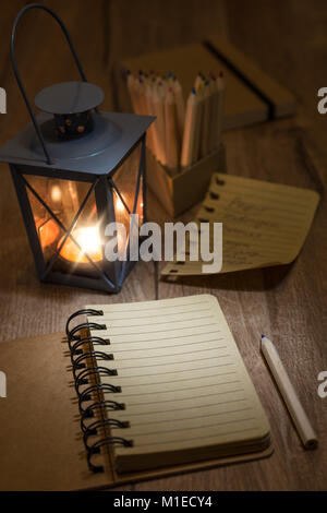 Open notebook with blank front page, candle in metal vintage lantern, torn-out page and a pencil on wooden table. Space for your notes, recipe or a po Stock Photo