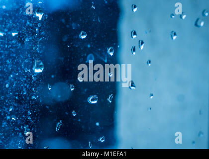 Raindrops on a (rather dirty) window. Blue dramatic sky in the background. With reflection of trees in the droplet. Stock Photo