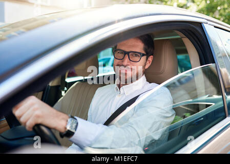 Smiling young man driving his car through the city streets Stock Photo