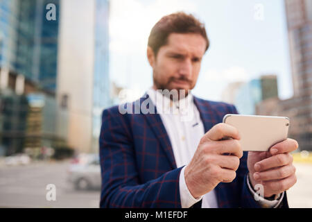 Young businessman using his smartphone while standing in the city  Stock Photo