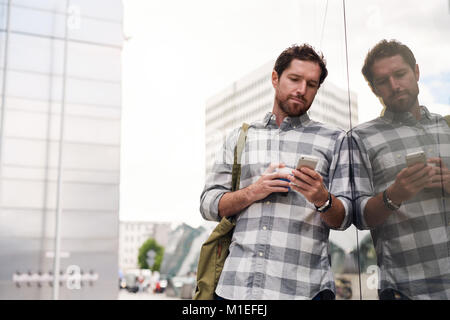 Young man standing in the city reading text messages Stock Photo