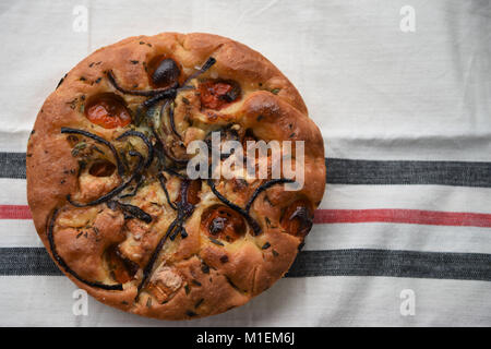 food of homemade focaccia bread topped with tomatoes red onion and goats cheese and laid on a cream table cloth for a rustic background Stock Photo
