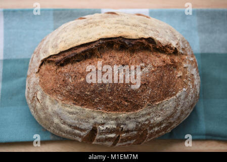 artisan food of a fresh home made and baked loaf of sourdough bread on a green cloth and wood board or table for a rustic image with overhead view Stock Photo