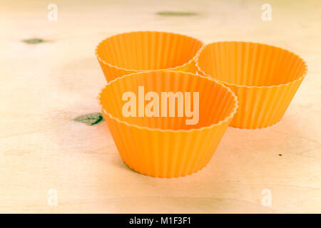 Orange silicone baking cups for muffins or cupcakes on solid wood background. Stock Photo