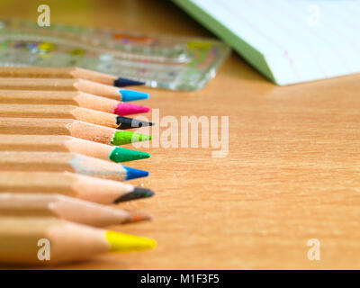 Colorful pencils on a writing desk, in the background figured ruler with notebook. Stock Photo
