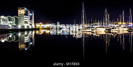 A view of various  pleasure craft reflected in mirror like water with apartment buildings visible on the waterfront. Stock Photo