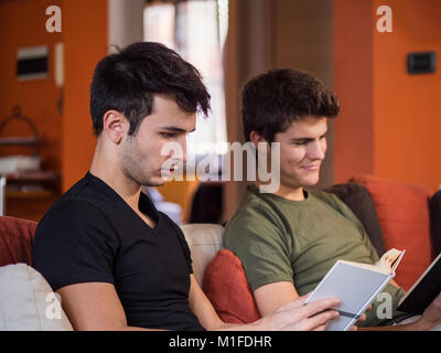 Two casual young men posing on couch concentrated on reading books at home. Stock Photo