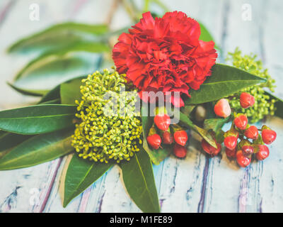 A bouquet of red and green flowers lying on a bluish wooden table shot against soft-focused background. Stock Photo