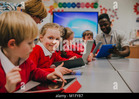 Primary school children are in the ckassroom, learning about and using digital tablets. One of the girls is smiling at the camera. Stock Photo