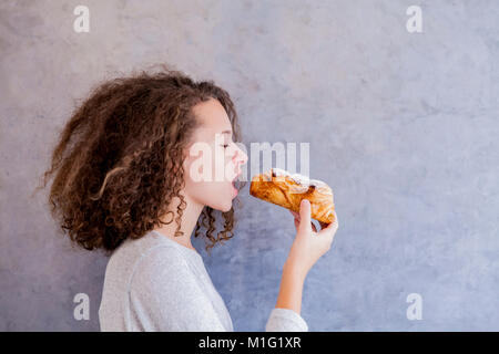 Portrait of curly hair teen girl eating croissant Stock Photo