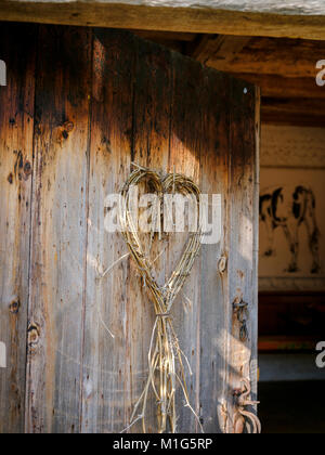 A rustic wooden barn door with a heart-shaped wreath hanging on it. Stock Photo