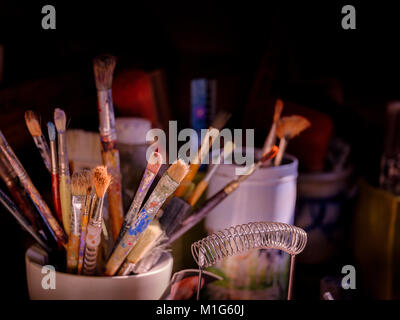 A set of paintbrushes in a studio lit with low angled window light to the side. Stock Photo