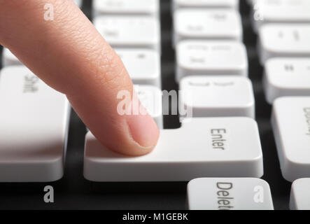 Finger pushing enter button on computer keyboard. Side view Stock Photo