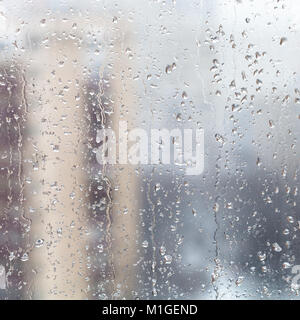 urban background - raindrops on home window glass (focus on water trickles on windowpane) in winter season Stock Photo