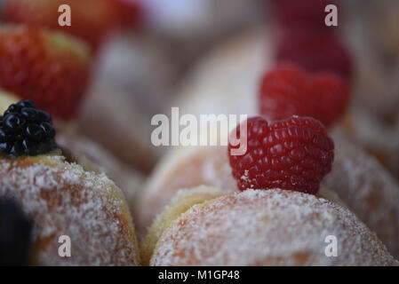 food image of some delicious fresh home made donuts or doughnuts coated in sugar with a jam filling and topped with a juicy red raspberry fruit Stock Photo