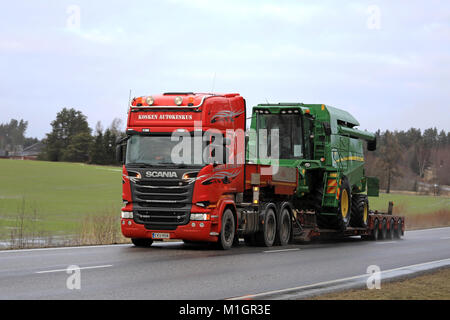 SALO, FINLAND - JANUARY 26, 2018: Scania R580 semi hauls John Deere W440 combine on gooseneck trailer as wide load along wet road on a rainy day in wi Stock Photo