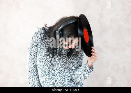 Young brunette pretty woman with vintage vinyl record on her head smiling while listening music Stock Photo