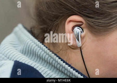 Close-up of woman ear with white earbud listenin to music. Stock Photo