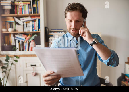 Man reading paperwork and talking on a cellphone at home Stock Photo