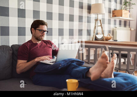 Young man lying on his sofa using a laptop Stock Photo