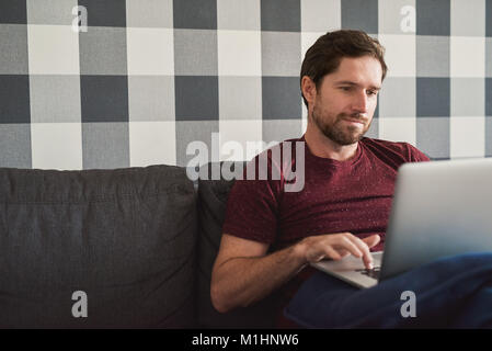 Young man relaxing on his sofa using a laptop Stock Photo