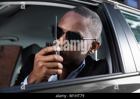 Surveillance Man With Sunglasses Sitting Inside Car Talking On Walkie Talkie Stock Photo