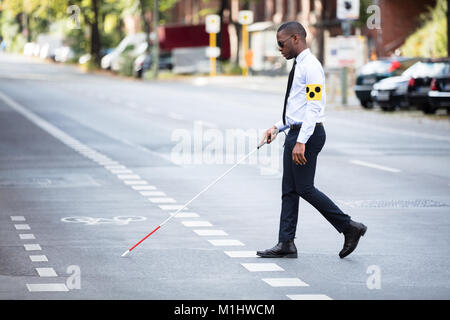 Young African Blind Man Wearing Armband Walking With Stick Crossing Road Stock Photo