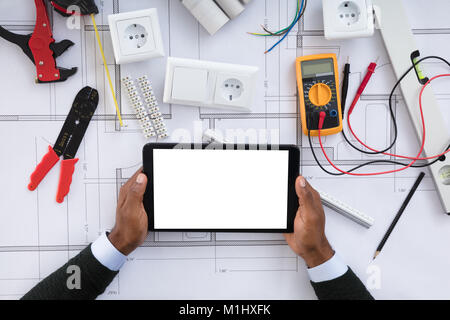Close-up Of A Person Holding Blank Screen Digital Tablet On Blueprint With Security Equipments Stock Photo