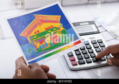 Close-up Of Person Hand Calculating Heat Temperature Using Calculator On Desk Stock Photo