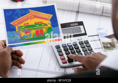 Close-up Of Person Hand Calculating Heat Temperature Using Calculator On Desk Stock Photo