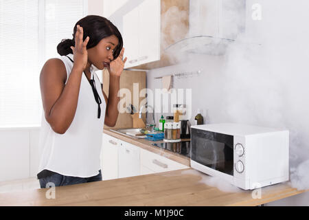 Shocked Young African Woman Looking At Burnt Pizza In Microwave Oven Stock Photo