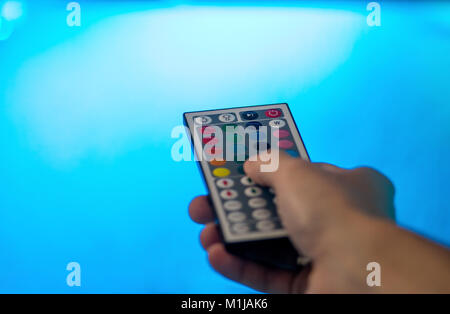 Hand holding a LED light remote control, changing light brightness, with a blue background from the LED illumination Stock Photo
