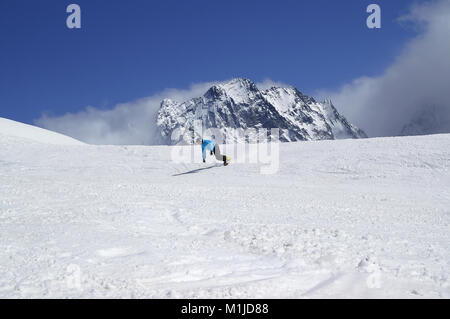 Snowboarder downhill in high snowy mountain at sun winter day. Caucasus Mountains, region Dombay. Stock Photo