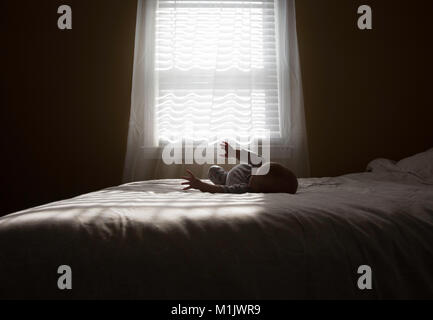 Baby Laying on Bed in front of Window Stock Photo