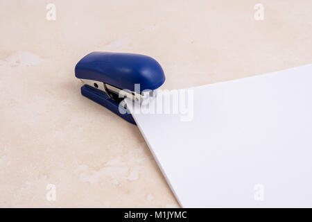Small blue stapler with paper on stone background Stock Photo