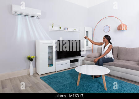 Happy African Woman Sitting On Sofa Using Air Conditioner At Home Stock Photo