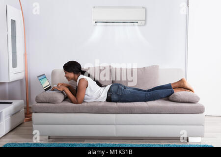 Young African Woman Lying On Sofa Watching Video On Laptop Stock Photo
