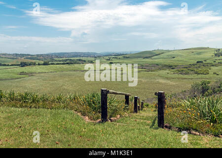 Wooden pole barrier fenced walkway , green vegetation and sugar cane plantations against distant Durban blue cloudy  skyline at Mount Moreland Stock Photo