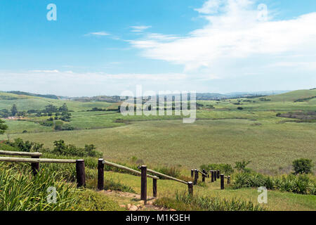 Wooden pole barrier fenced walkway , green vegetation and sugar cane plantations against distant Durban blue cloudy  skyline at Mount Moreland Stock Photo