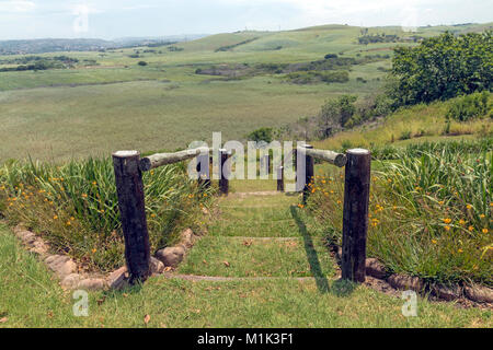 Wooden pole barrier fenced walkway , green vegetation and sugar cane plantations against distant Durban blue cloudy  skyline at Mount Moreland Stock Photo