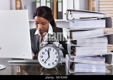Young African Businesswoman Working In Office With Clock And Stacked Folders On Desk Stock Photo