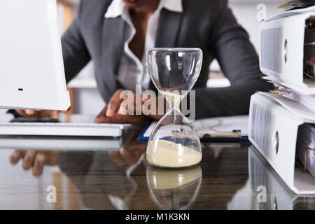 Close-up Of Hourglass In Front Of Businessperson Working In Office Stock Photo