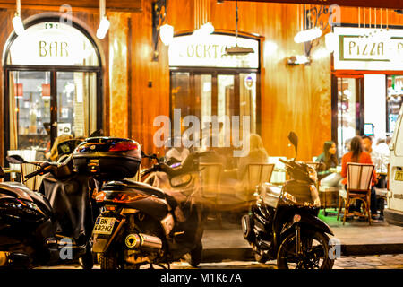 Late night in Paris France at a sidewalk cafe and bar in the Latin Quarter with motorcycles out front and diners enjoy a meal as tourists walk by Stock Photo