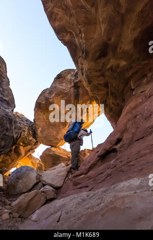 Hiker climbing a route through a sandstone fin within Salt Creek Canyon in The Needles District of Canyonlands National Park, Utah, USA Stock Photo